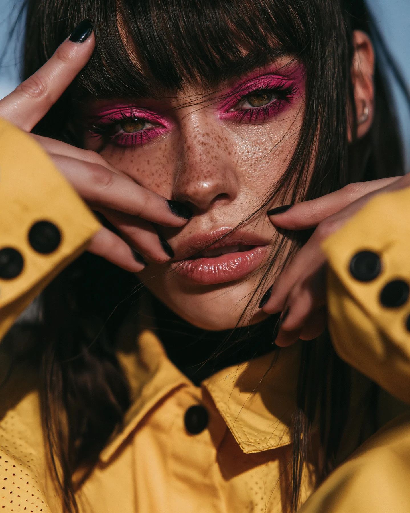 A close portrait framed by yellow sleeves, with pink eye makeup.